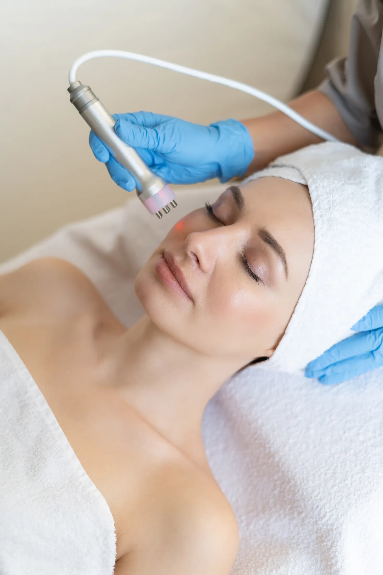 Soin du visage à l’appareil sur une cliente allongée, serviette blanche