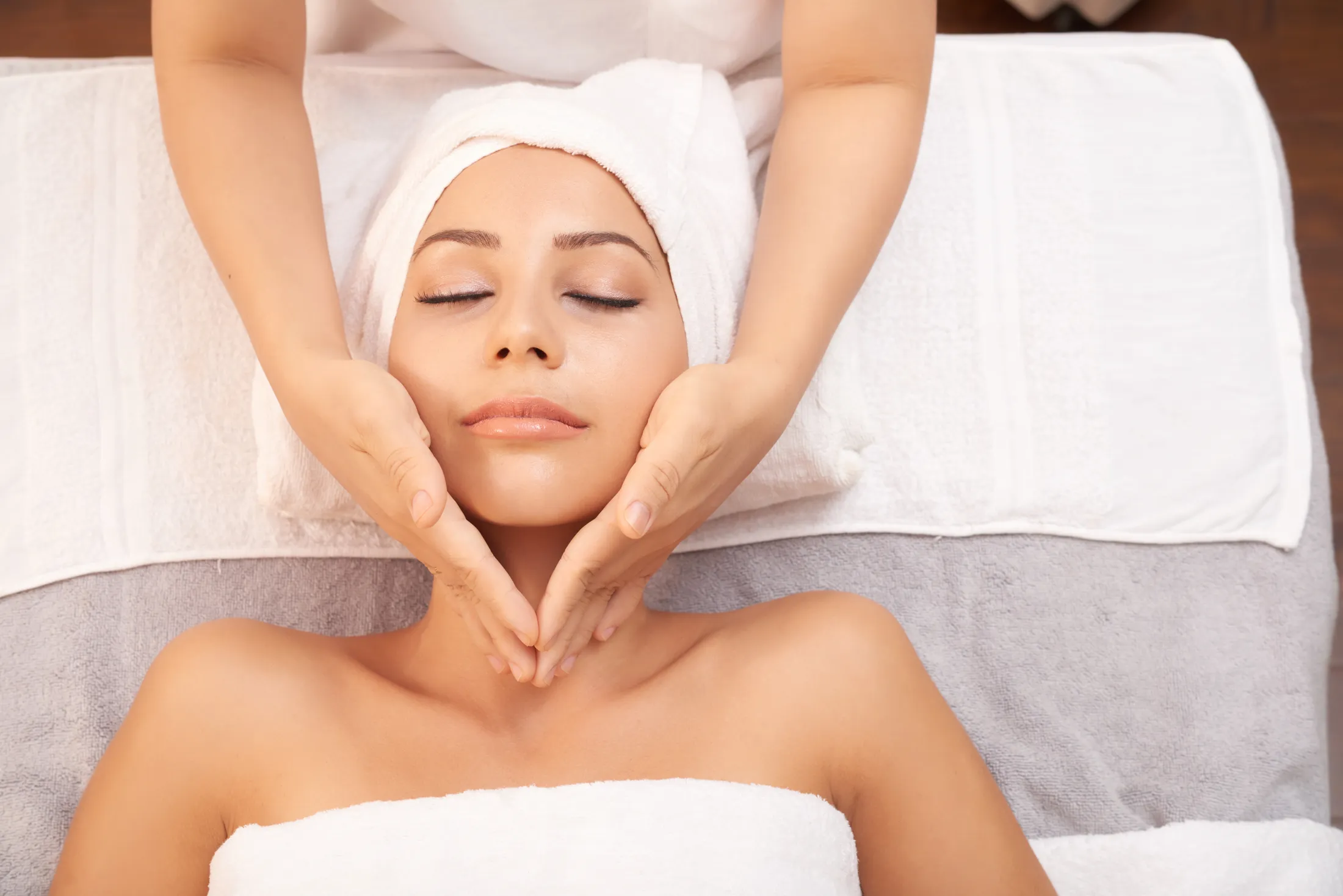 Mains d’esthéticienne qui massent le visage d’une cliente détendue