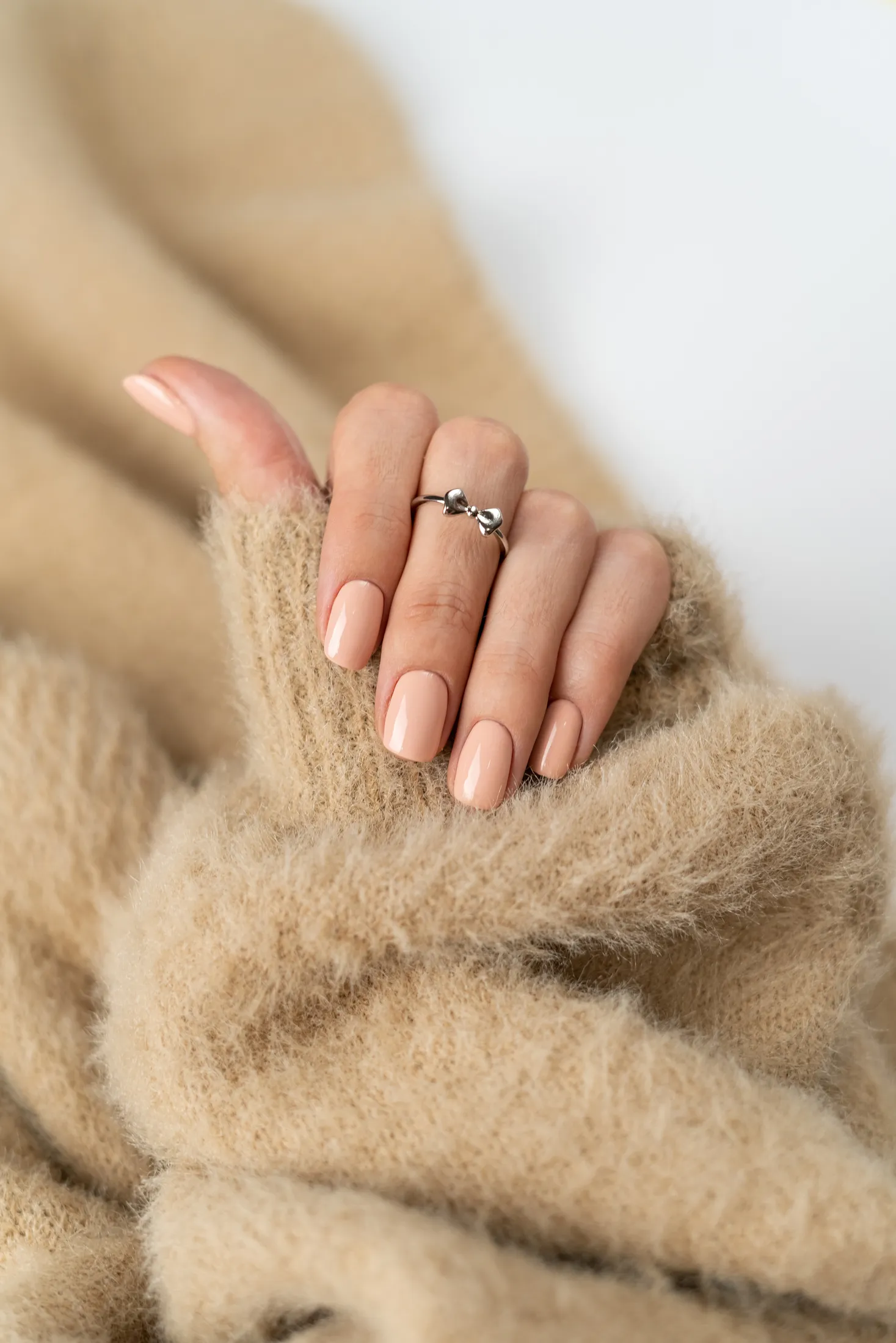 Manucure nude sur des doigts fins, posés sur un pull doux